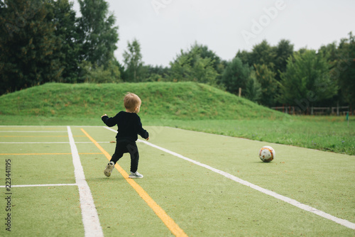 Cute one-year-old kid playing soccer with a ball on artificial grass