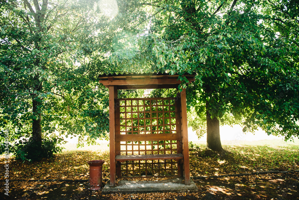 Wooden summerhouse in the park in the summer.. Outdoor wooden gazebo over summer landscape background Wooden summerhouse in the park in the summer.. Outdoor wooden gazebo over summer landscape background