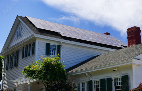 Solar panels on the roof of a traditional Colonial style house beneath a blue summer sky