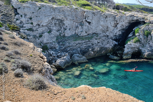 Puglia, Italy, August 2018, Cala Tonda in the wild north coast of SAn Domino island in a sunny day. A canoeist admires the beauty of the place.