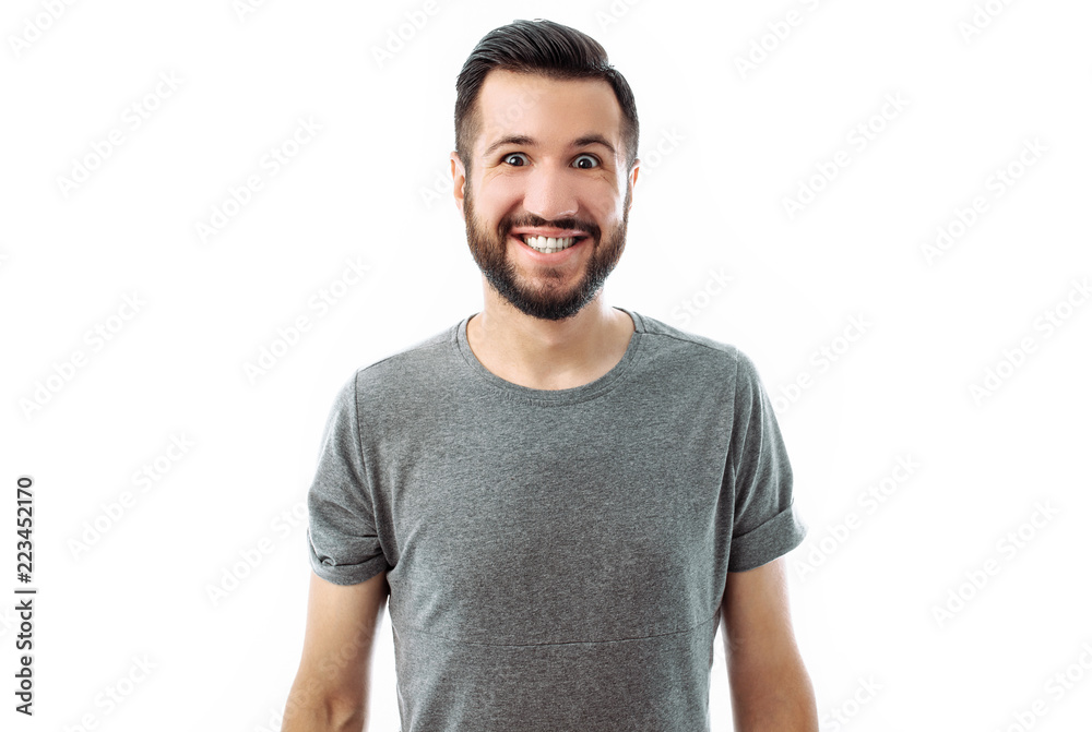 Portrait of a young man with a beard, wearing a gray shirt posing for the camera with a big smile on a white background Portrait of a young man with a beard, wearing a gray shirt posing for the camera with a big smile on a white background