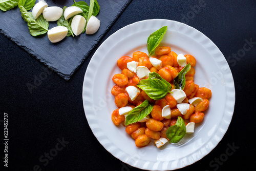 Gnocchi alla Sorrentina in tomato sauce with green fresh basil and mozzarella balls served on a plate photo