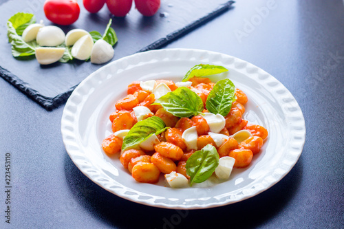 Gnocchi in tomato sauce with green fresh basil and mozzarella balls served on a plate. Italian recipe