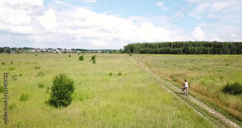 Pushkin district, Moscow region, Russia - July 7, 2018. Young adult woman riding a bicycle on a rural road. Aerial view