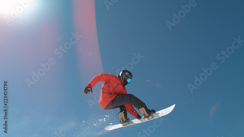 SLOW MOTION: Extreme snowboarder jumping across the clear blue sky in winter