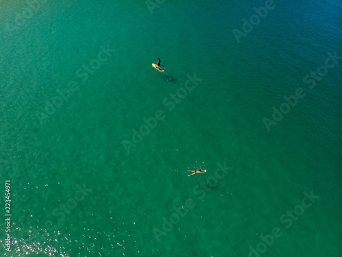  The aerial view of unrecognizable people rises paddle boarding on the surface of the water for sport, and fun. Enjoy the summer SUP activity for holidays. © Nedrofly