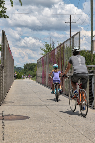 Unidentifiable people biking across a bridge on the Atlanta Beltline on a bright summer day with a blue sky and white clouds