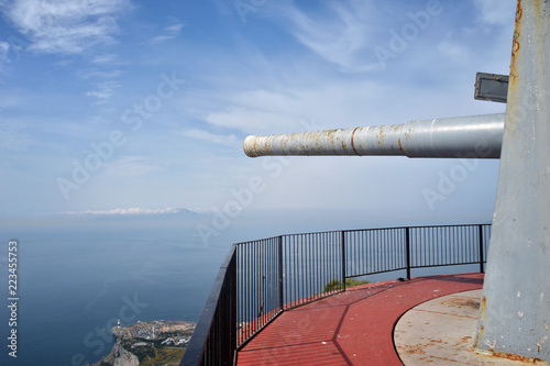 Vista View of rusty old World War II weapon overlooking the sea with lighthouse below and blue skies