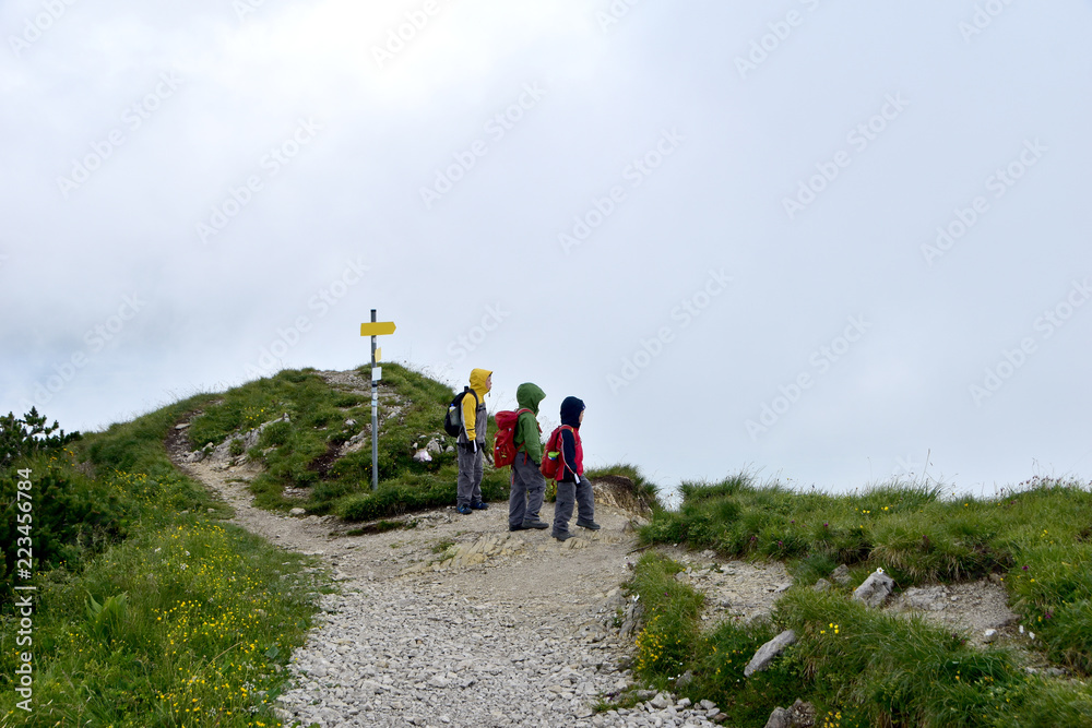 Obraz premium Three young children with backpacks and waterproof jackets ready for adventure on a hiking trail.