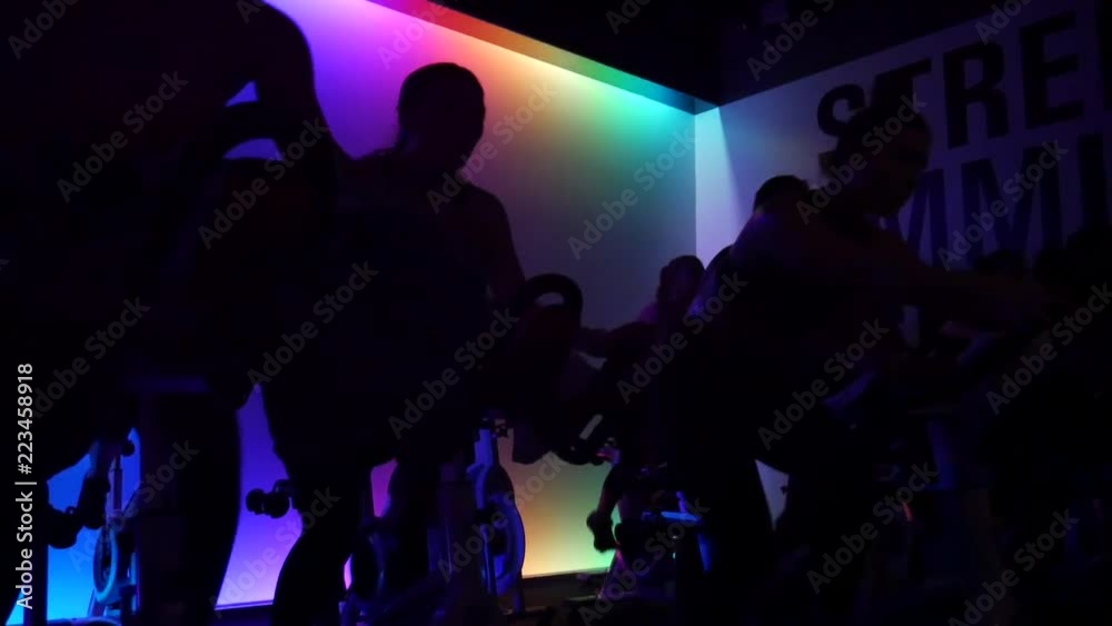 Participants in spin class ride stationary bikes in the dark with pulsating lights.