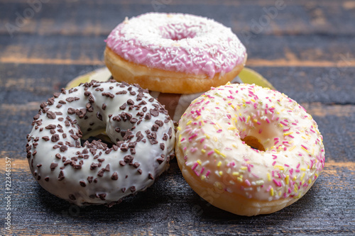 Colorful sweet glazed donuts from bakery on black wooden background close up