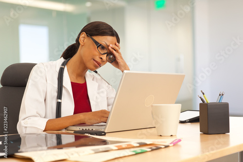 Stressed young female physician using laptop computer at work