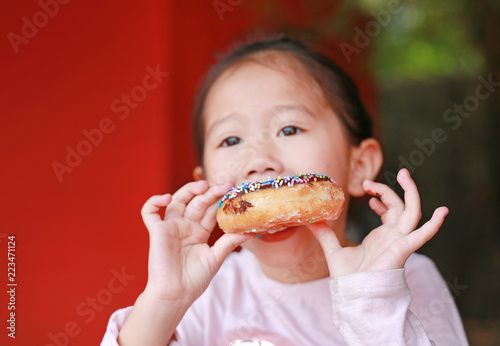 Portrait of child girl enjoy eating rainbow donut.