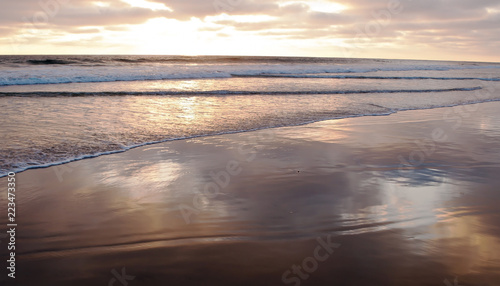 A southern California  USA sunset with the sky and clouds reflecting off the shallow ocean water and wet sand on the beach