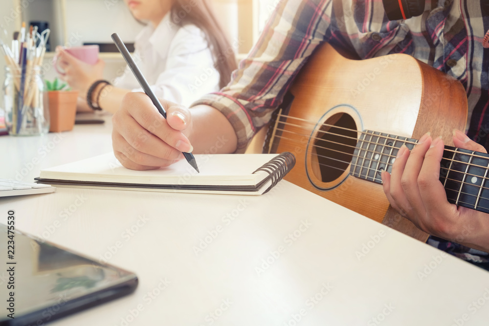 Fototapeta premium Cropped shot musician artist working on workplace with guitar on hand and holding a pencil writing on notebook paper,song writer concept.