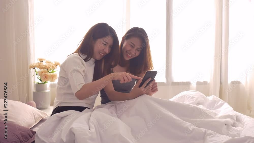 Beautiful young asian women LGBT lesbian happy couple sitting on bed hug and using phone together bedroom at home. LGBT lesbian couple together indoors concept. Spending nice time at home. Beautiful young asian women LGBT lesbian happy couple sitting on bed hug and using phone together bedroom at home. LGBT lesbian couple together indoors concept. Spending nice time at home.
