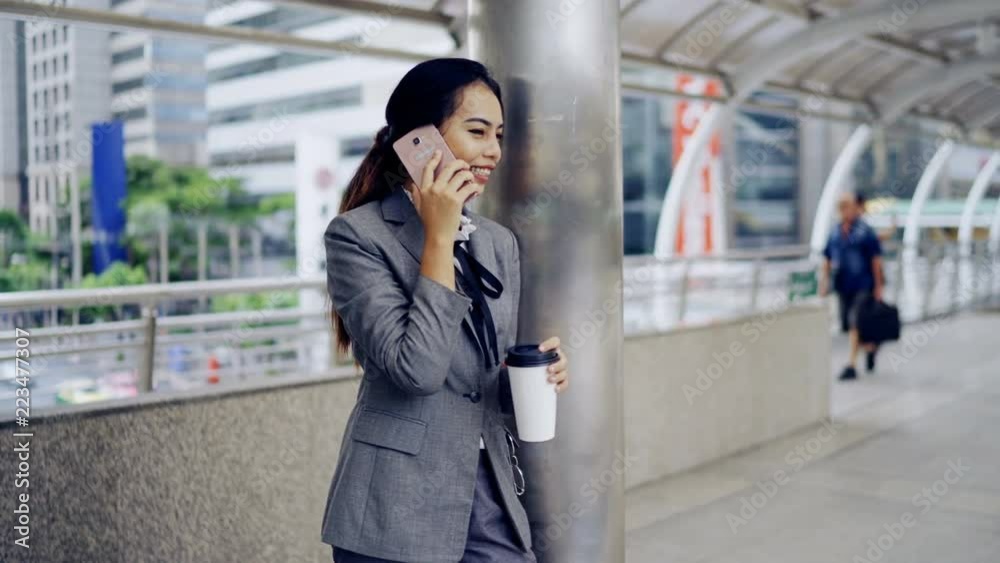 Asian businesswoman standing outside the office and talks on her mobile phone Asian businesswoman standing outside the office and talks on her mobile phone