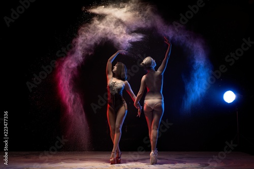 Fototapeta Naklejka Na Ścianę i Meble -  Two girls dancing in color dust cloud in the dark