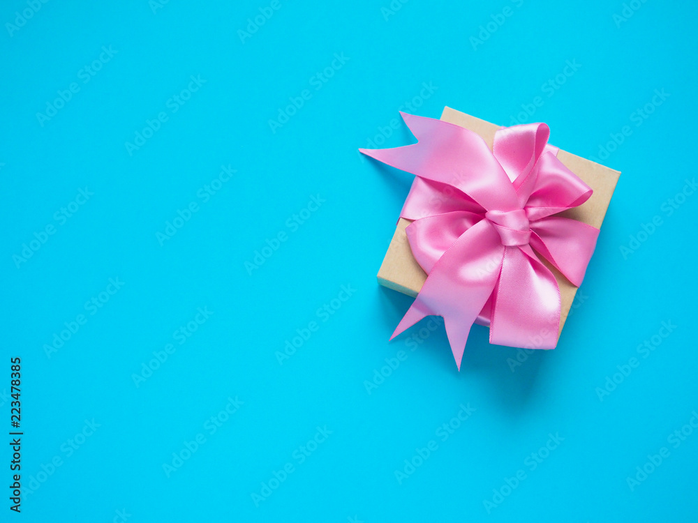 one gift box with pink satin ribbon on a blue background, copy space for text one gift box with pink satin ribbon on a blue background, copy space for text