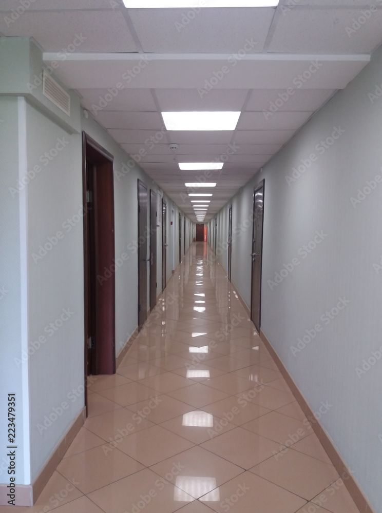 A long white hall with dark wood doors and a mirror-bright floor.