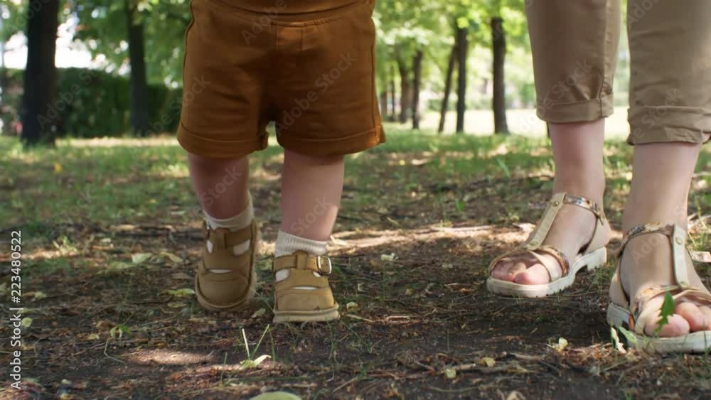 Tracking with low-section of legs of woman and toddling baby walking together in park Tracking with low-section of legs of woman and toddling baby walking together in park