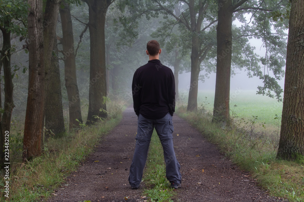 Young man standing on path in morning misty fog from back Young man standing on path in morning misty fog from back