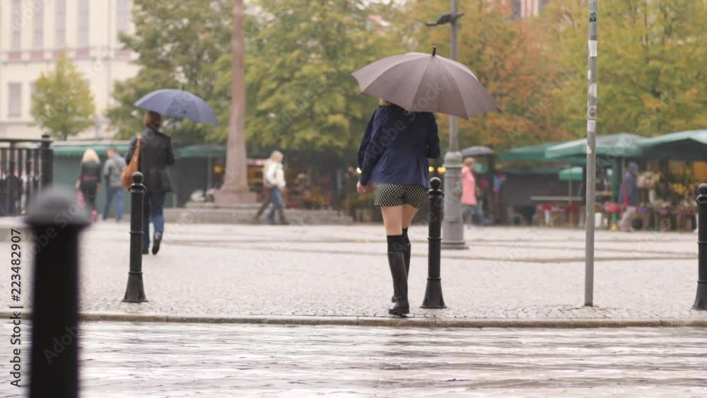 Woman in rainy weather in rubber boots run across a road pedestrian crossing under umbrella Woman in rainy weather in rubber boots run across a road pedestrian crossing under umbrella