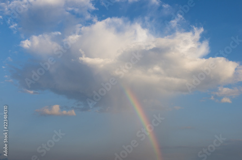 The blue sky and the big cloud with rain and the rainbow that glows from it © Kseniia