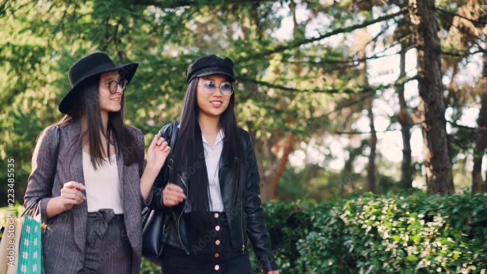 Beautiful girls hipsters are walking in the street with paper bags and talking on sunny autumn day in city. Shopping together, friendship and leisure concept. Beautiful girls hipsters are walking in the street with paper bags and talking on sunny autumn day in city. Shopping together, friendship and leisure concept.