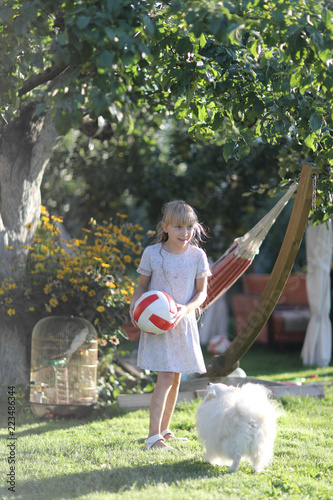 Wallpaper Mural Blond girl playing in the yard of the house with a ball and a little furry dog of the breed of spitz Torontodigital.ca