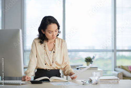 Young Chinese business lady reading documents on her table