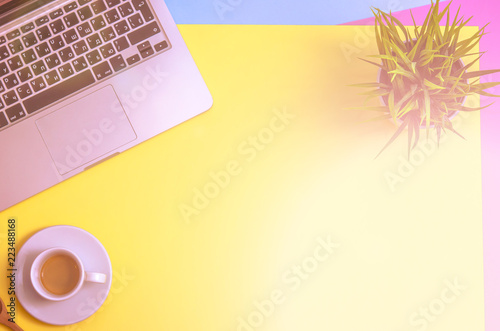 Laptop and clipboard with coffee and plant on yellow, blue and purpure background. Morning. Flat lay. Top view. Copy space