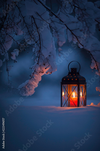 Candle lantern under the snowy branches at dusk. Christmas time in a wintery garden.