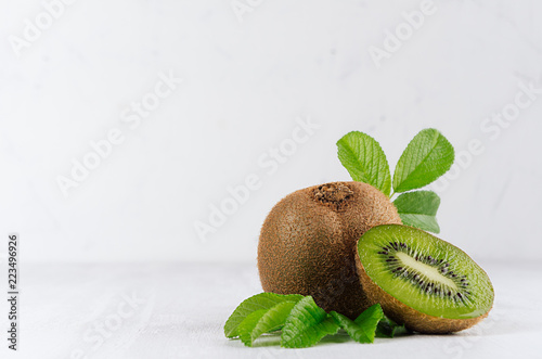 Exotic fruts  closeup - juicy ripe fleshy kiwi with slice, drop juice and young green leaves in elegant white kitchen interior. photo