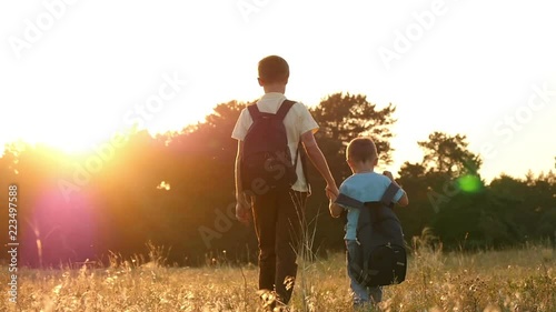 Two brother of a tourist walking with backpacks, holding hands. Happy children are walking in nature on a sunset background. photo