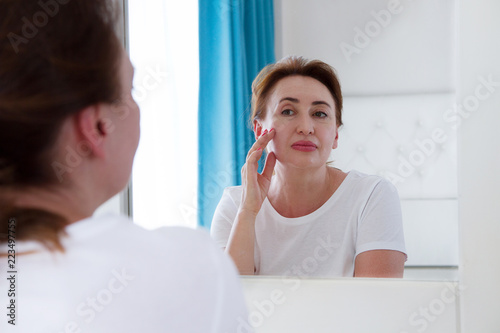 Photos Middle age woman looking in mirror on face