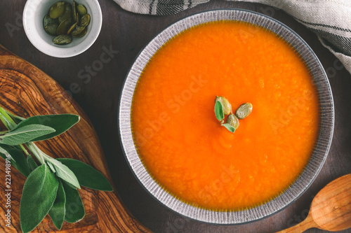 Season pumpkin creamy soup with sage in a rustic kitchen. Homemade recipe, top view, vertical orientation.