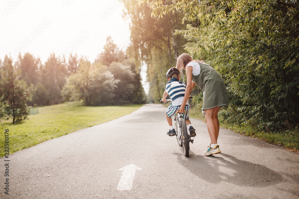 Fototapeta premium Sister and little brother learning to ride bicycle park having fun together