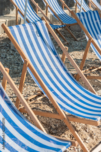 Blue and white wooden Deckchairs on a sandy beach opened. ready for sunbathing.