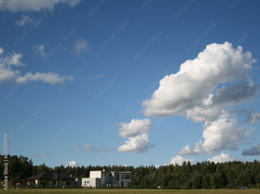 view on white house and forest and sky with clouds in sunny summer day