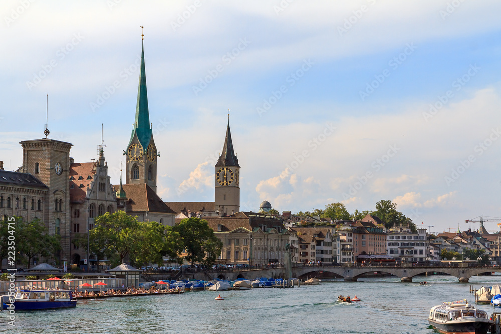 Beautiful summer cityscape of Zurich, Switzerland, at the river Limmat with women swimming in the Frauenbad Stadthausquai and the Fraumünster and St. Peter Churches
