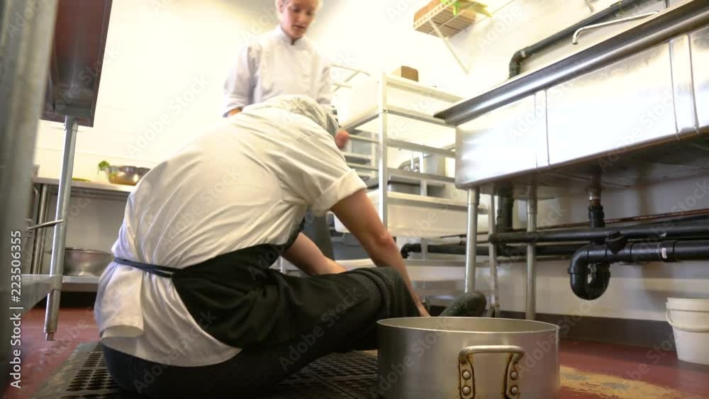 A chef or food service worker trips and falls in a kitchen injuring himself.  A coworker comes to his assistance.