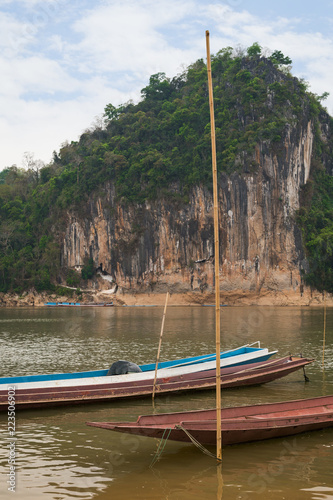 Moored boats on the Mekong River in front of a limestone cliff where the famous Pak Ou Caves are set. They are located near Luang Prabang in Laos. photo