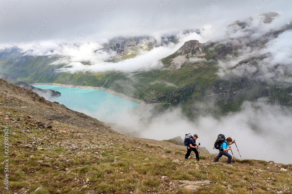 A couple with backpacks hiking on a summer day in the Swiss alps near Grimentz, Switzerland, with turquoise lake lac de Moiry in the background, on July 27, 2014

