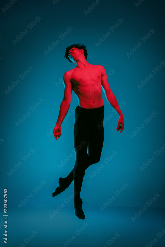 The male athletic ballet dancer performing dance on dark blue background. Studio shot. Ballet concept. Fit young man. Caucasian model