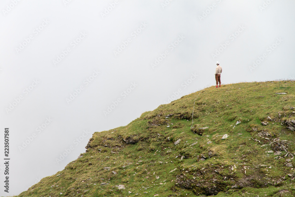 Young man standing on the edge of a cliff in the swiss alps with a valley full of clouds near Grimentz, Switzerland, in summer
