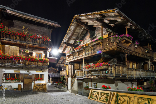 Beautiful traditional houses in the streets of the village Grimentz, Switzerland, canton Valais, municipality Anniviers, at night with geranium flowers on the balconies illuminated by streetlights