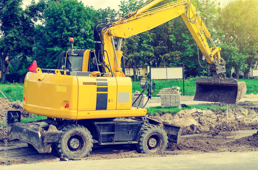 Large yellow excavator digs a hole, repairs the road, heavy equipment, road works.