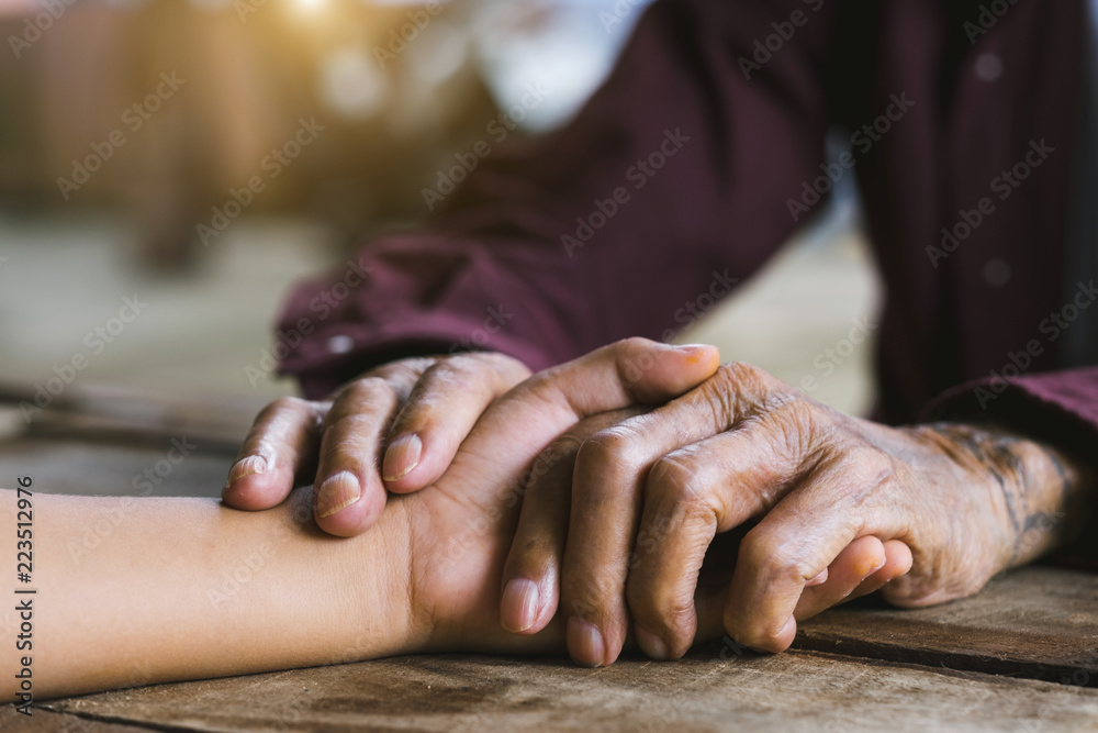Fototapeta premium Hands of the old man and a child's hand on the wood table