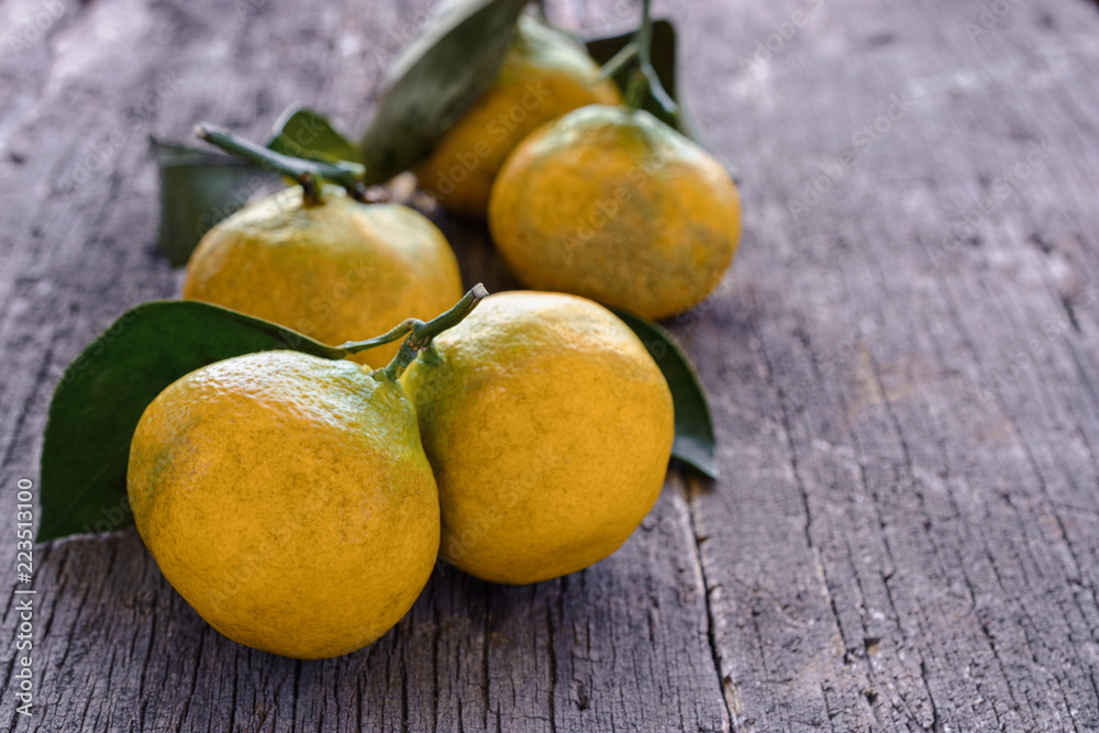 Row of juicy, ripe mandarin orange (tangerines) with a yellowish-greenish peel and green leaves are on the old board